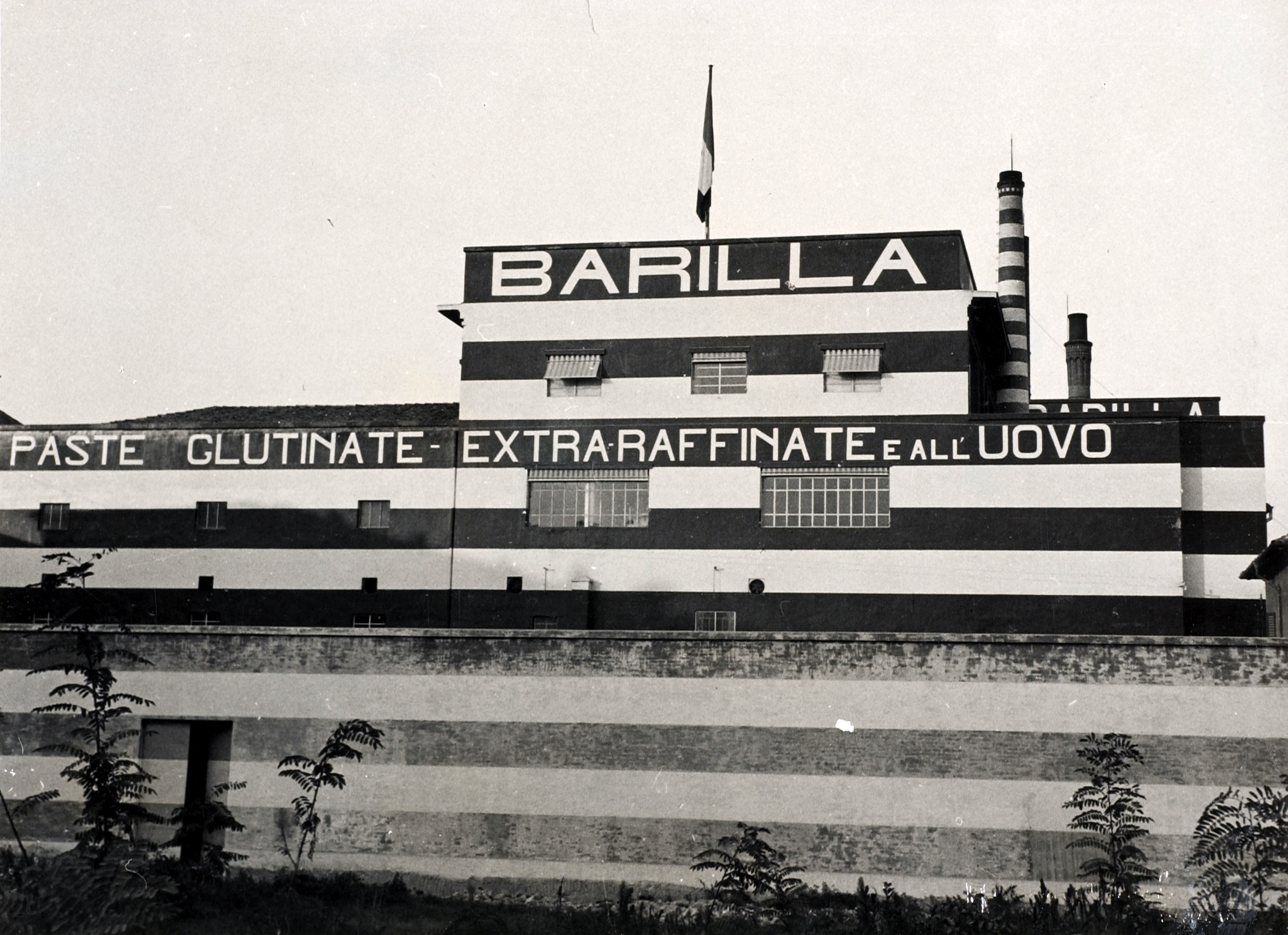 Il fronte verso Sud dello stabilimento, caratterizzato dalle insegne dipinte e da un trattamento cromatico a fasce bianche e rosse, in una foto del 1930 [ASB, A 106].